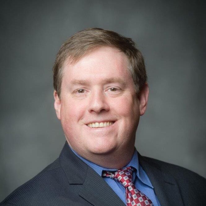 A man in a suit and tie smiling for the camera.