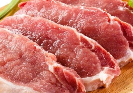 A close up of raw meat on top of a wooden cutting board.