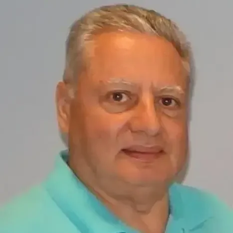 A man with blonde hair and glasses wearing a blue shirt.